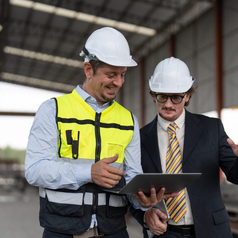 Businessman and male engineer walking and discussing the project making precast concrete wall at construction site.